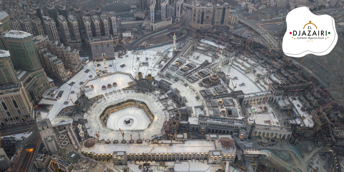 Vue aérienne panoramique de la Grande Mosquée d'Al-Haram à La Mecque, avec en superposition le logo du restaurant 'El Djazairi - Authentic Algerian Food'. L'image illustre la présence de la cuisine traditionnelle algérienne à proximité des lieux saints pour les pèlerins.