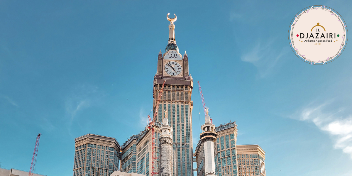 Photographie de la tour de l'horloge Abraj Al Bait à La Mecque sous un ciel bleu, avec le logo du Restaurant El Djazairi en incrustation, mettant en avant les saveurs authentiques de la cuisine algérienne au cœur de la ville sainte.