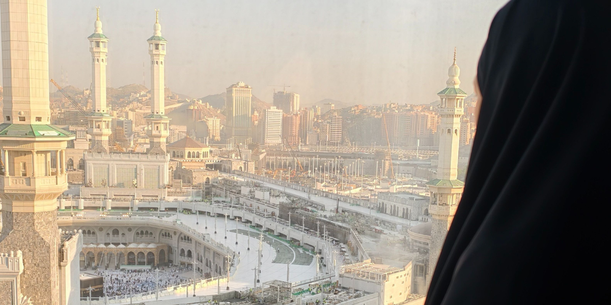 Une femme observe la mosquée Al-Haram depuis une fenêtre, illustrant la paix et les récompenses de la omra de la femme.