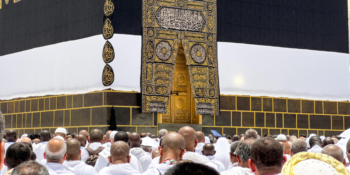 Une foule de pèlerins en habit d'Ihram rassemblés devant la porte dorée de la Kaaba à La Mecque. L'image souligne l'aspect communautaire et sacré du pèlerinage, représentant le service de Omra par procuration pour faire bénéficier un défunt des mérites de ce lieu saint.