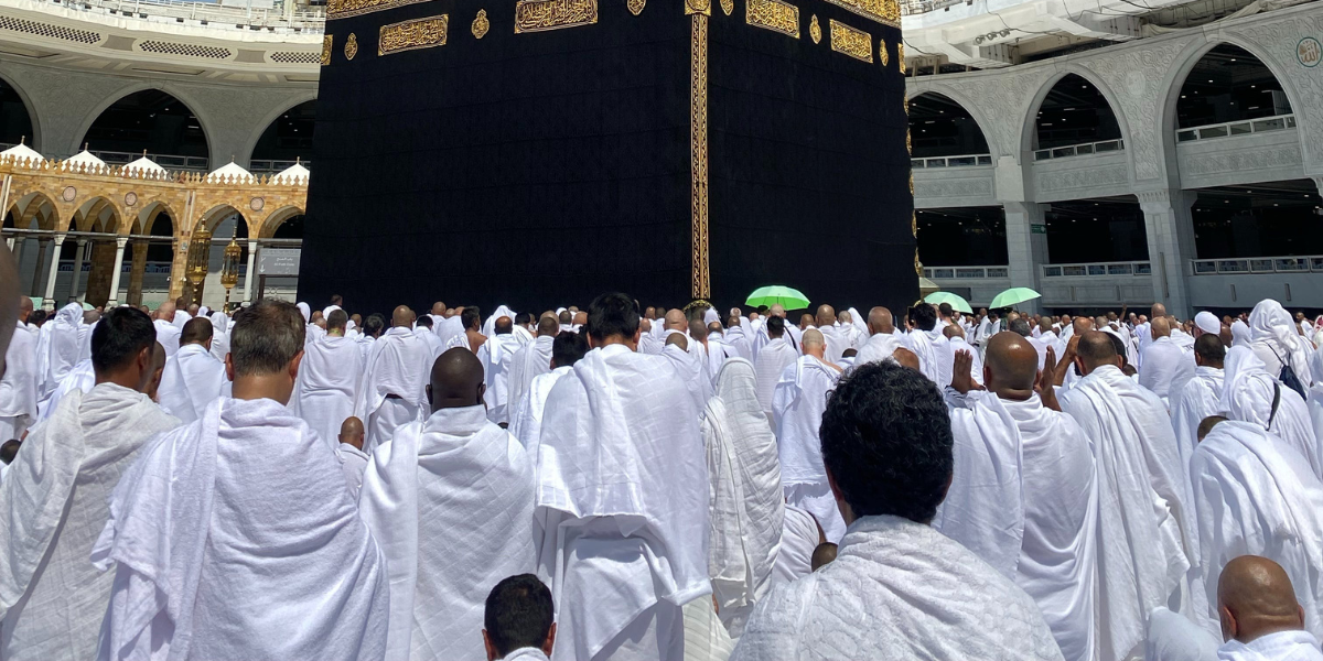 Une assemblée de fidèles en habit d'Ihram devant la Kaaba à Masjid al-Haram, représentant le sérieux et la piété de l'équipe Direct Mecca lors de la prise en charge de votre demande de Omra par procuration.