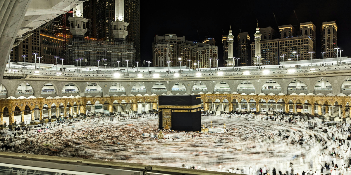 Omra de Lyon avec Turkish Airlines : voyage spirituel à La Mecque Vue nocturne panoramique de la Kaaba à La Mecque avec une foule de pèlerins effectuant le Tawaf en mouvement, symbolisant le voyage de la Omra au départ de Lyon avec Turkish Airlines.