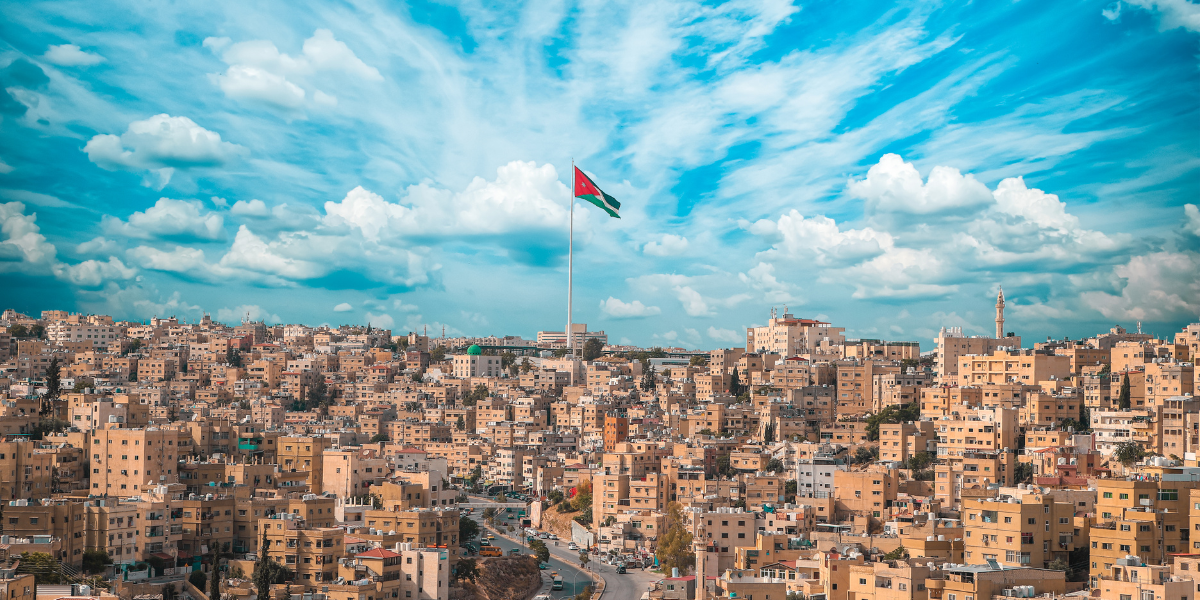 Vue panoramique sur la ville d'Amman avec le drapeau national, illustrant l'escale stratégique avec Royal Jordanian.