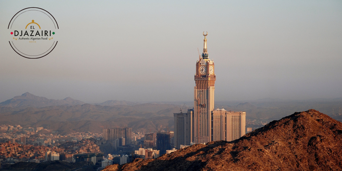 Vue panoramique de la Tour de l'Horloge à La Mecque avec le logo El Djazairi, illustrant la restauration authentique à proximité du Haram.
