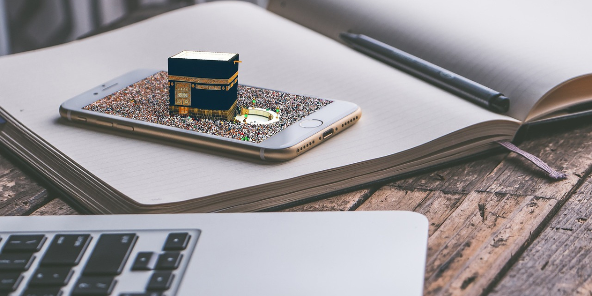 Smartphone affichant la Kaaba posé sur un carnet et un ordinateur portable, illustrant la réservation experte et la gestion complète de votre voyage par Direct Mecca.