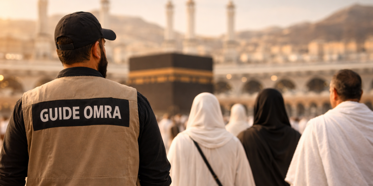 Guide Omra pas à pas : une assistance experte pour un pèlerinage en toute sérénité Plan rapproché de dos d'un accompagnateur portant un gilet beige avec l'inscription "GUIDE OMRA". Il accompagne un groupe de pèlerins vers la Kaaba au sein de la Grande Mosquée de La Mecque, illustrant le soutien logistique et spirituel.