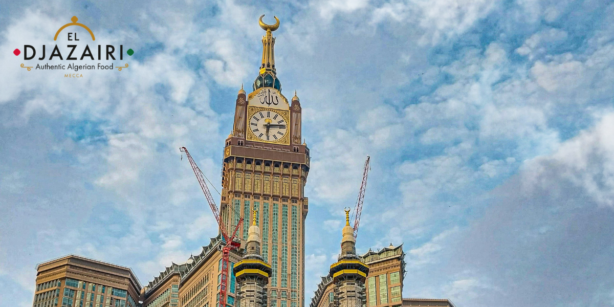 Vue de la Makkah Clock Tower sous un ciel nuageux avec le logo du restaurant El Djazairi, symbolisant la restauration algérienne authentique pour les pèlerins à La Mecque.