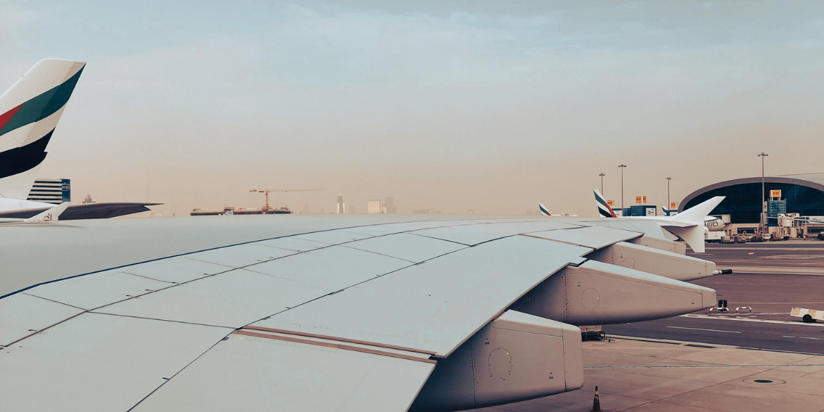 Vue sur le tarmac de l'aéroport montrant l'aile d'un avion et plusieurs avions de la compagnie Emirates, illustrant l'escale et la logistique du voyage pour une Omra au départ de Lyon.