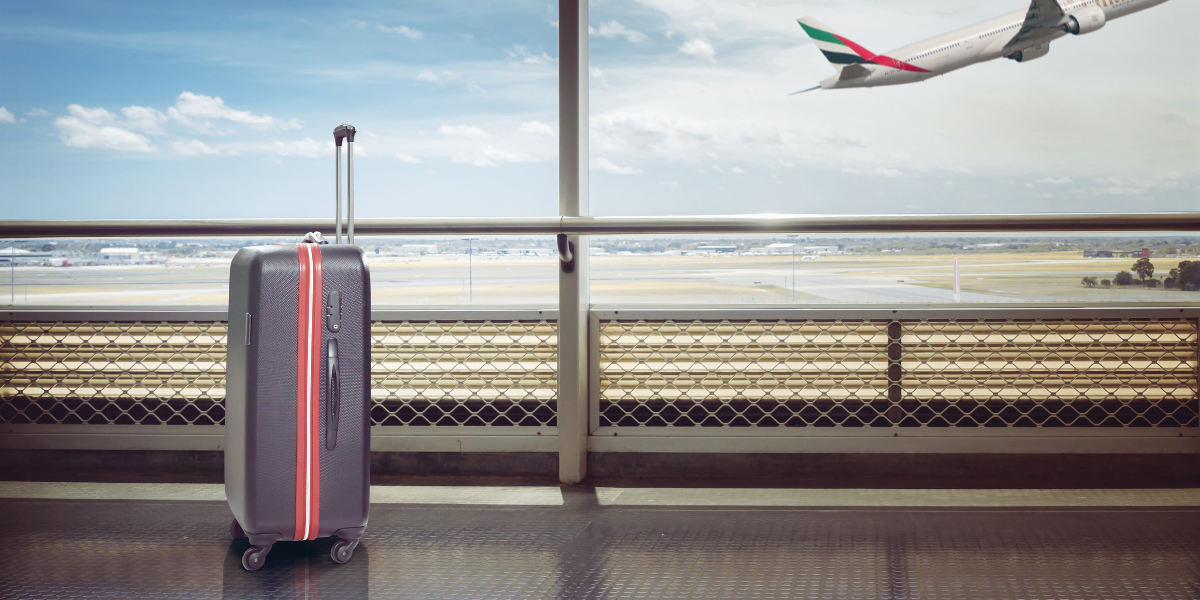Une valise seule à l'aéroport avec un avion Emirates décollant en arrière-plan, symbolisant la prise en charge des bagages et la tranquillité d'esprit pour un pèlerin au départ de Lyon.