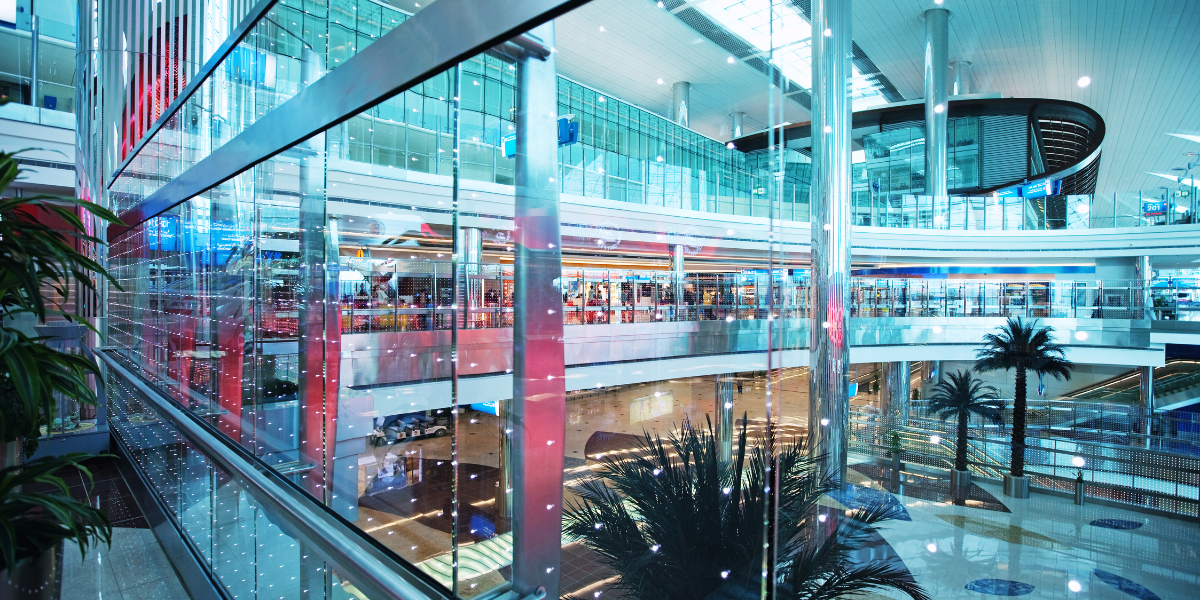 Vue panoramique de l'intérieur lumineux et moderne du Terminal 3 de l'aéroport de Dubaï, montrant les palmiers d'intérieur et les structures en verre, illustrant un transit fluide pour les pèlerins en route vers la Omra.