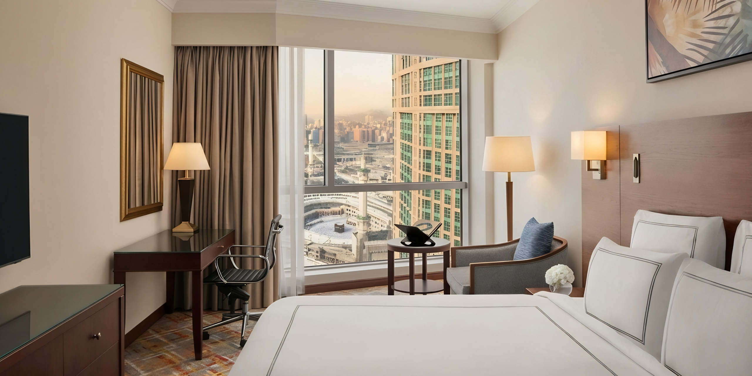 Chambre d'hôtel 5 étoiles luxueuse et épurée avec une large fenêtre ouvrant sur une vue panoramique de la Kaaba et du Masjid al-Haram, illustrant l'hébergement de prestige sélectionné par le guide Omra premium.