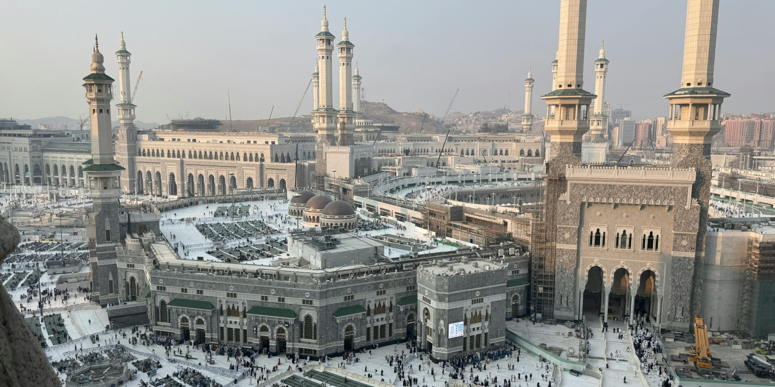 Vue panoramique en hauteur du vaste complexe de la Mosquée al-Haram à La Mecque, montrant ses nombreux minarets et ses esplanades, illustrant l'immensité du site pour aider à choisir entre un guide privé et une agence classique lors d'une Omra en solo.