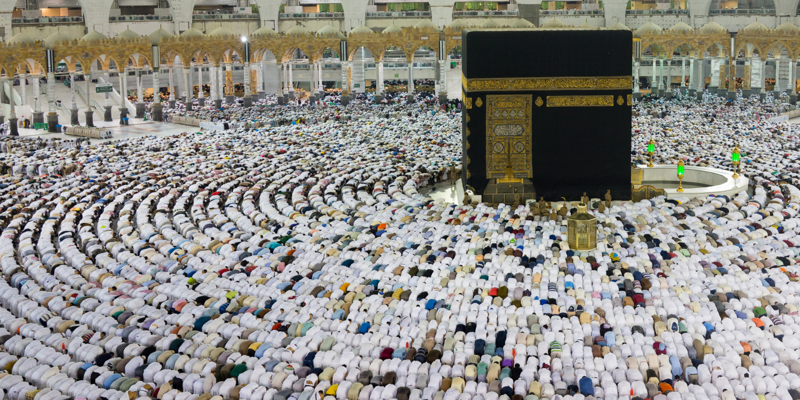 Vue en plongée de la Kaaba à La Mecque, entourée de rangées circulaires parfaites de pèlerins prosternés en prière sur l'esplanade, illustrant le rôle d'un accompagnement fraternel et discret pour réussir son Tawaf et son Sa'y lors d'une Omra en solo.