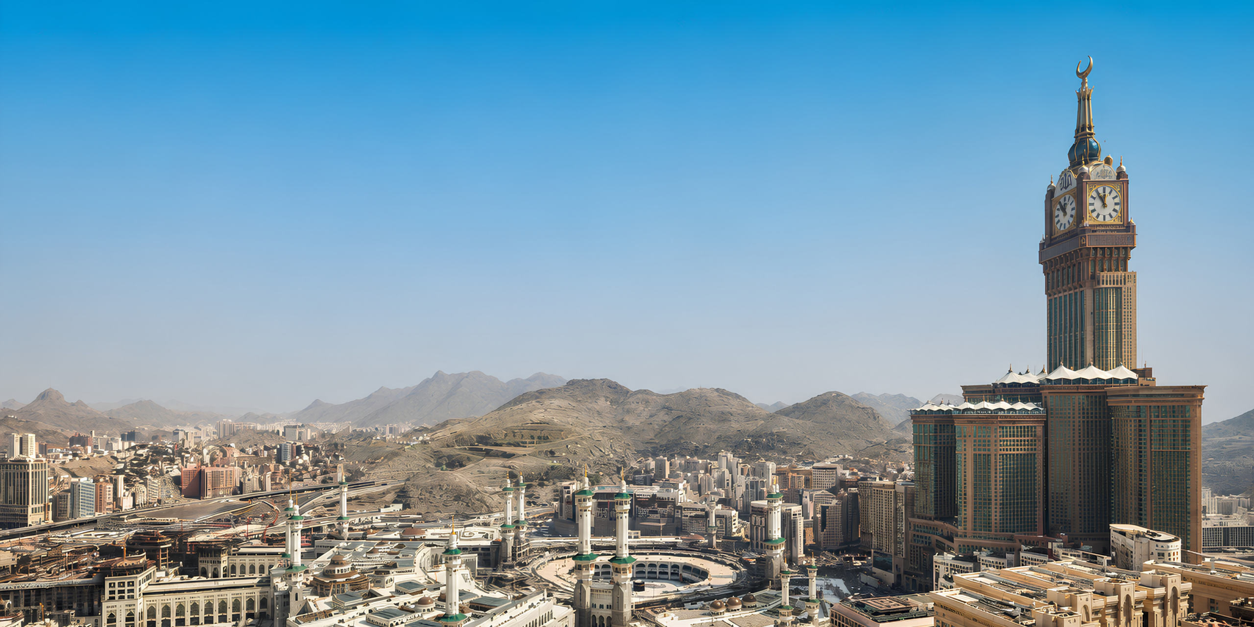 Une vue panoramique de la ville de La Mecque en plein jour sous un ciel bleu dégagé, mettant en valeur la célèbre tour de l'horloge (Makkah Clock Tower) dominant l'esplanade du Haram et les montagnes environnantes, illustrant les conditions climatiques estivales et les visites incontournables.