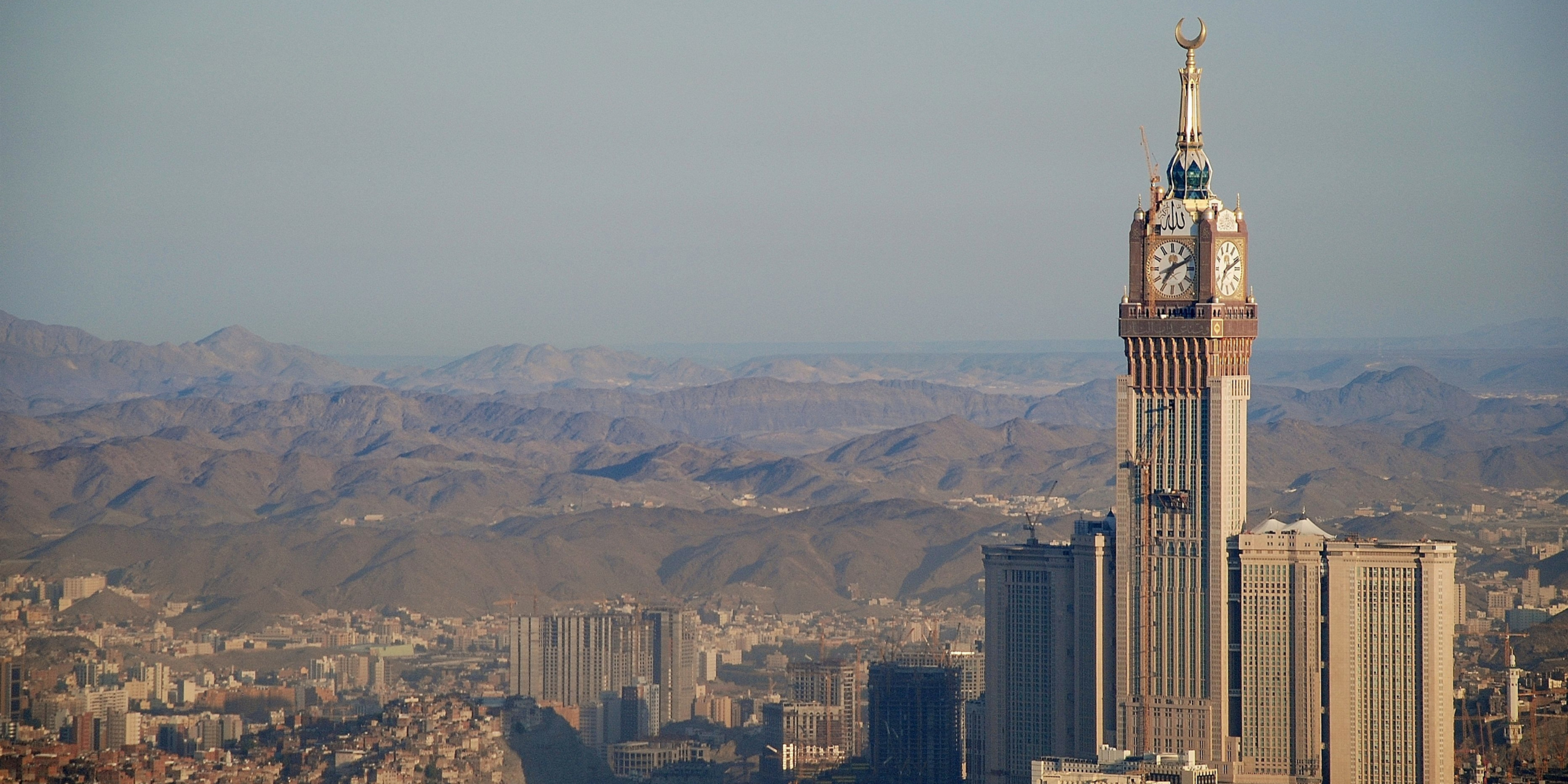 La Tour de l'Horloge (Makkah Clock Tower) dominant la ville de La Mecque avec les montagnes arides en arrière-plan, illustrant les questions fréquentes sur la durée et la période idéale pour une première Omra.