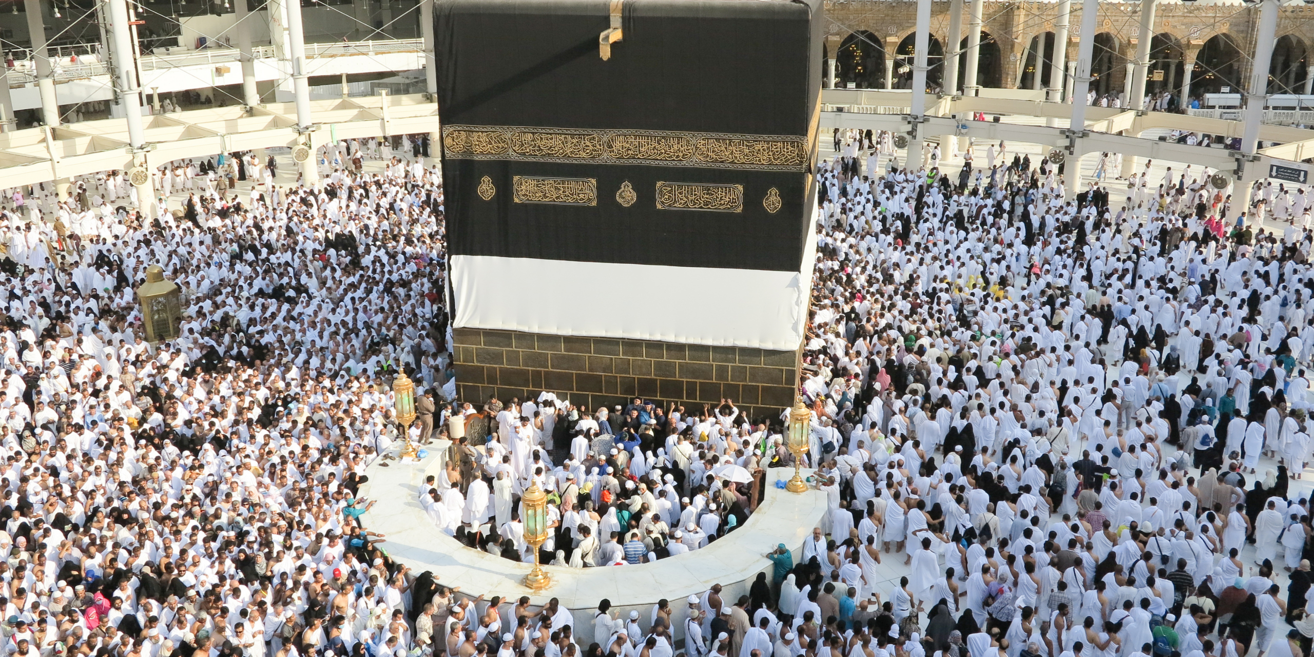 Vue rapprochée de la Kaaba drapée de sa Kiswah et entourée d'une foule dense de pèlerins, illustrant l'importance de se préparer physiquement et mentalement avant le voyage à La Mecque.