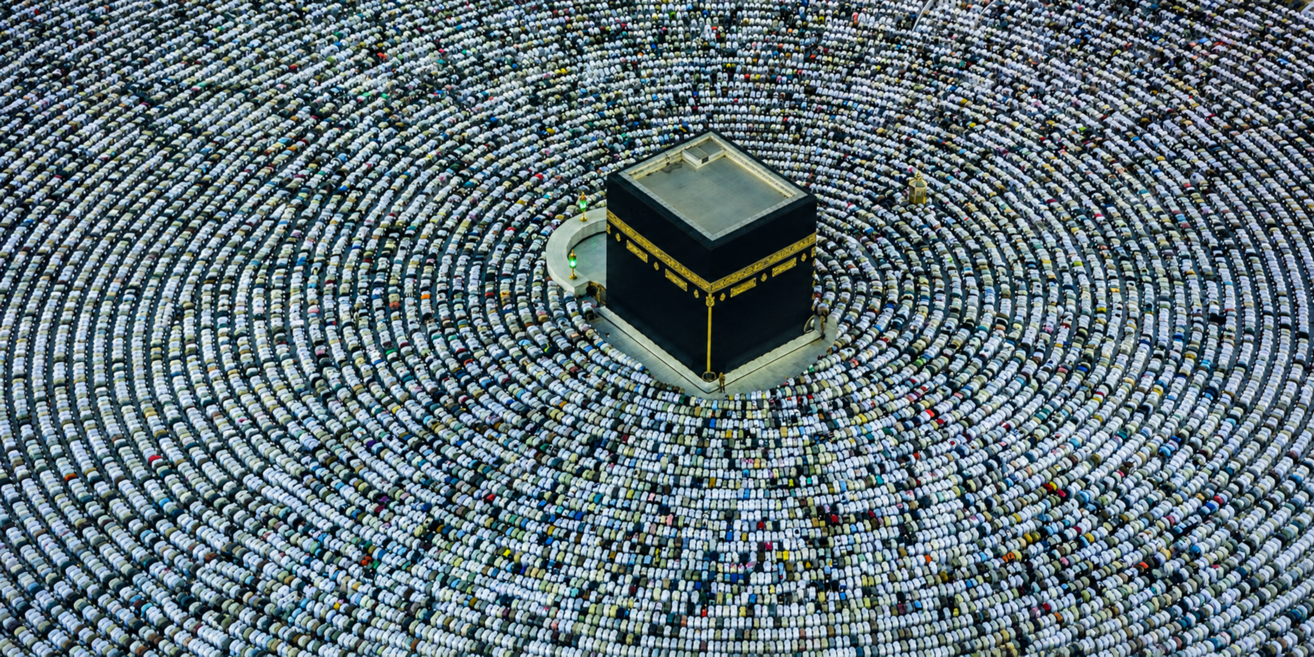 Une vue aérienne spectaculaire prise directement au-dessus de la Kaaba, montrant des milliers de pèlerins alignés en cercles concentriques parfaits tout autour du monument pour la prière dans la cour de la Grande Mosquée de La Mecque, illustrant la maîtrise des rituels et des invocations enseignée par le guide Omra express.