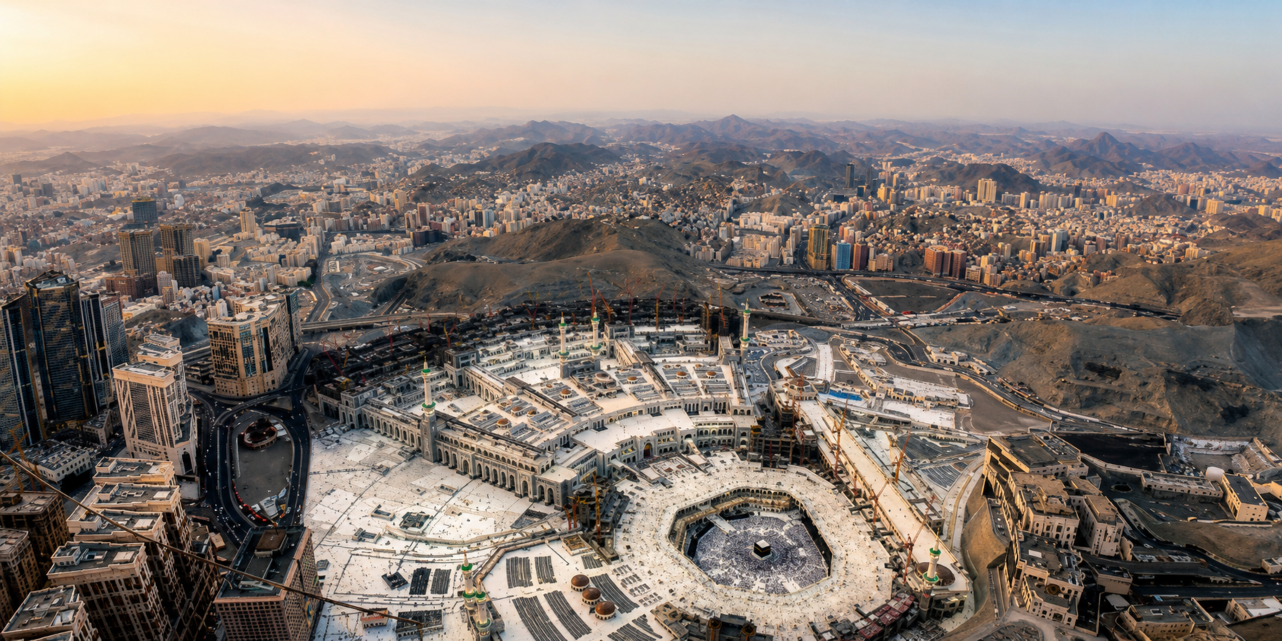 Une vue panoramique en hauteur montrant l'immensité du complexe de la Grande Mosquée de La Mecque et la Kaaba au centre, entourée par le relief montagneux et la ville, illustrant la planification globale et le suivi rigoureux du programme de la Omra étape par étape, depuis le départ jusqu'aux visites guidées.