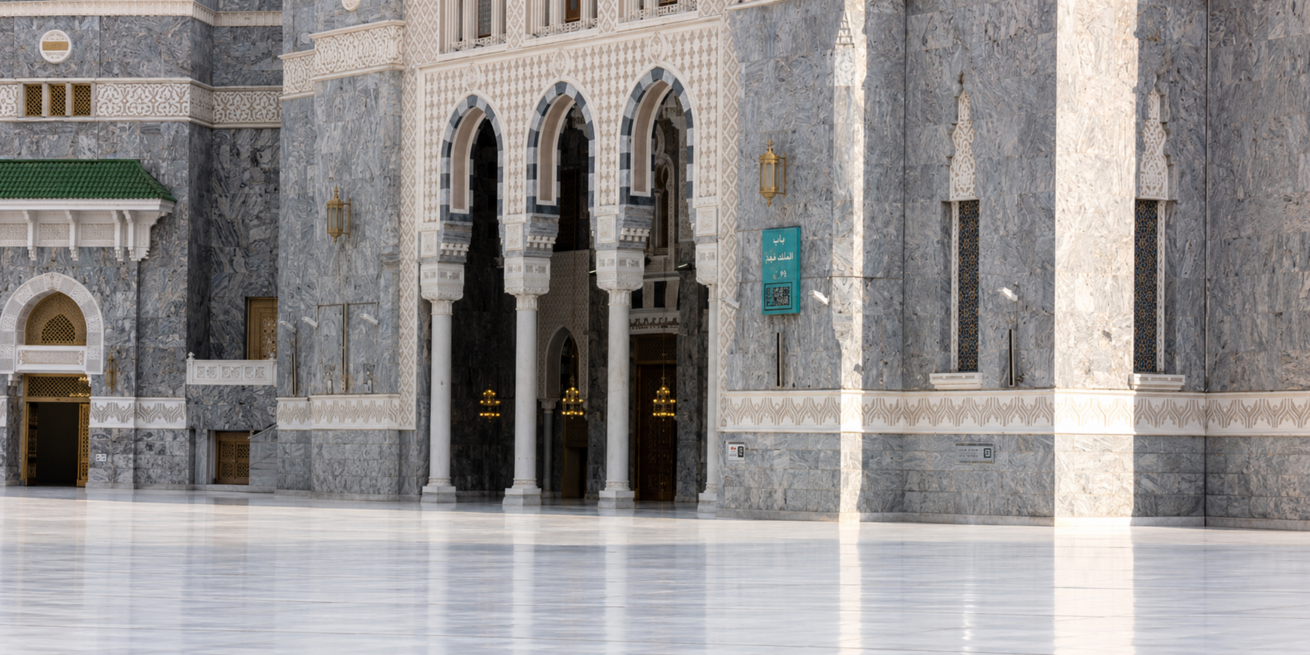 Une vue sur l'architecture monumentale et les grandes arches en marbre de l'une des entrées de la Grande Mosquée de La Mecque (porte du Roi Fahd), donnant sur une esplanade extérieure vide et propre, illustrant la sécurité, la sérénité et la logistique simplifiée à proximité immédiate du Haram.