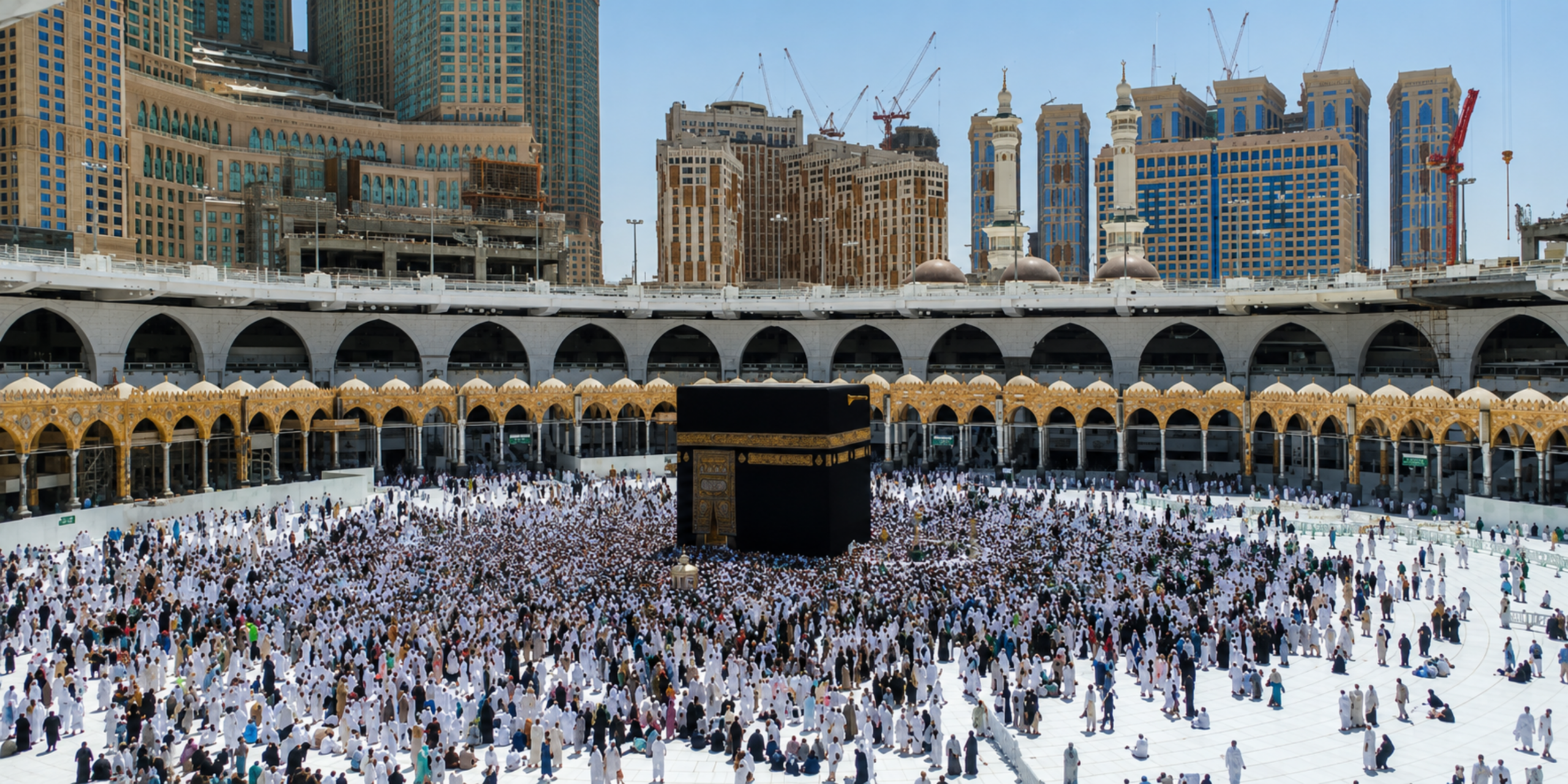 Une large vue en contre-plongée montrant la Kaaba sacrée au centre du Mataf entouré de pèlerins, encadrée par la colonnade dorée et les arcades de la Grande Mosquée sous les grands immeubles de La Mecque, illustrant l'opportunité d'effectuer son pèlerinage en famille durant le mois d'août 2027.