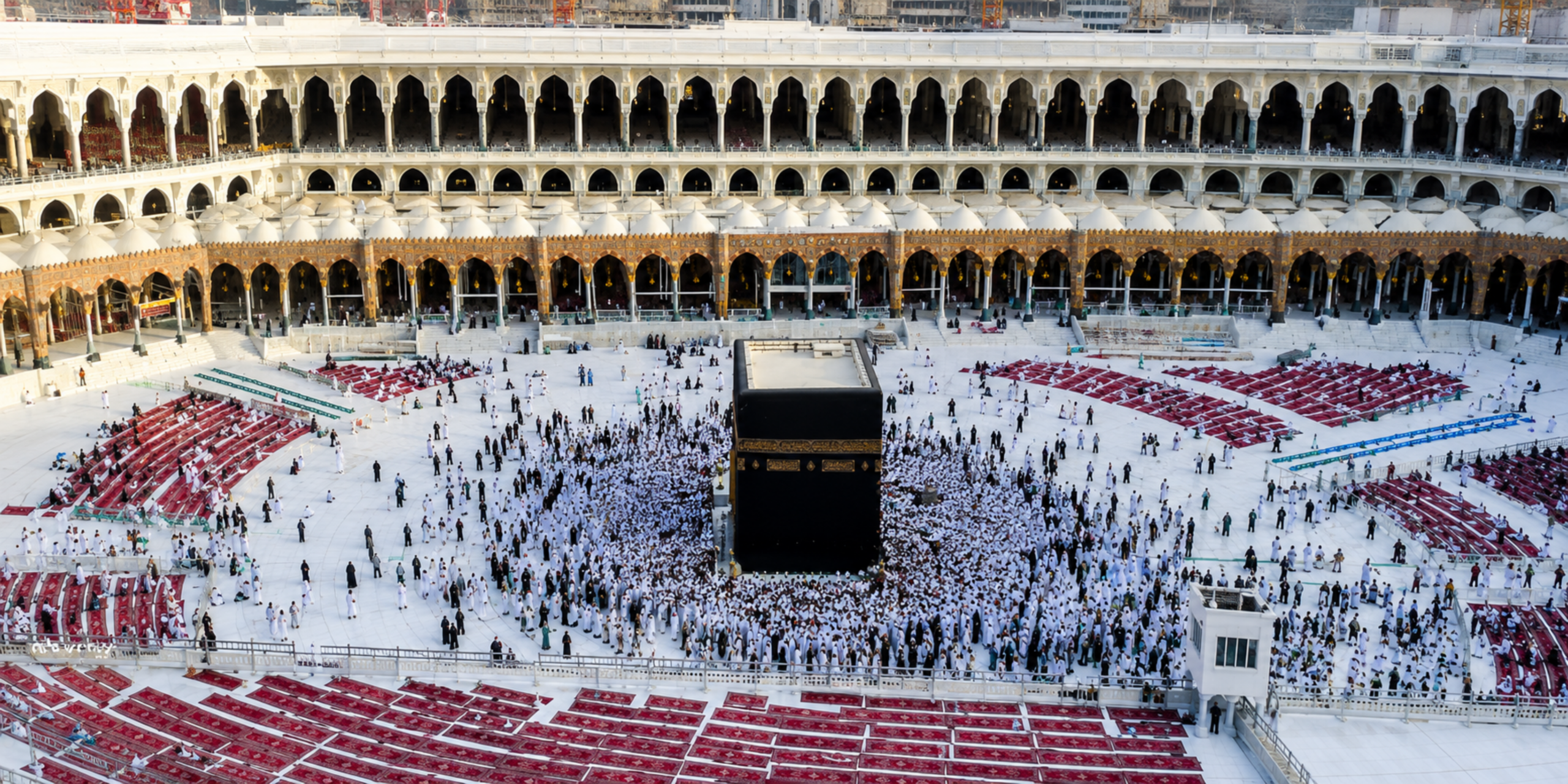 Vue en contre-plongée plongeante sur le Mataf de la Mosquée Al-Haram, montrant la Kaaba sacrée entourée de pèlerins effectuant le Tawaf, encadrée par les tapis de prière rouges alignés et les arcades de la cour, illustrant les avantages d'une réservation anticipée pour sa Omra en août 2027.