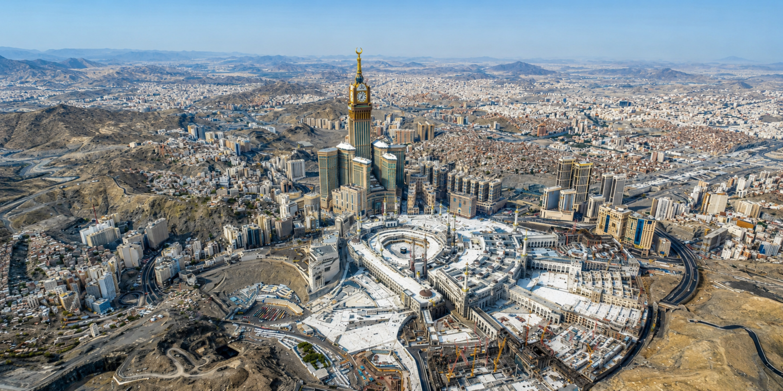 Vue aérienne panoramique de la ville de La Mecque, montrant le complexe de la Grande Mosquée Al-Haram au centre entouré par les infrastructures hôtelières et la Tour de l'Horloge, illustrant la planification des tarifs, des formules et du budget global pour une Omra en août 2027.
