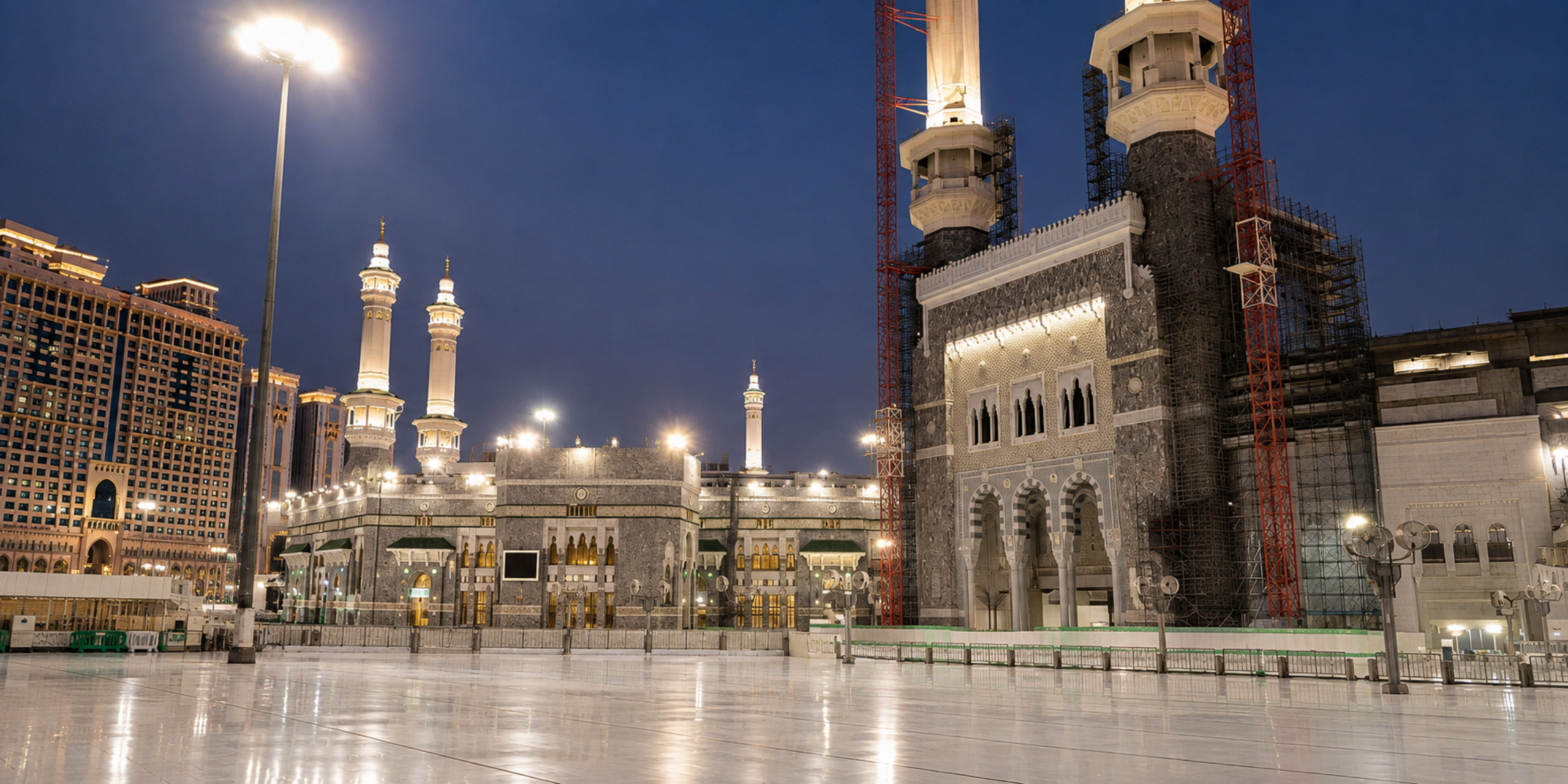Une vue nocturne sur l'esplanade extérieure éclairée de la Grande Mosquée de La Mecque, montrant l'architecture majestueuse des façades, des minarets et des grands portaux sous un ciel de nuit, illustrant la garantie, la fiabilité et la réservation d'un séjour Omra personnalisé pour le Ramadan 2027 avec Direct Mecca.