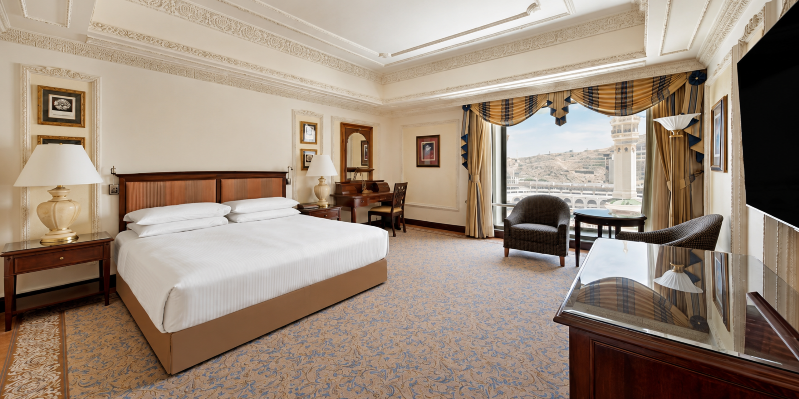 Une spacieuse chambre de luxe dotée d'un grand lit double, d'un coin salon élégant et d'une grande fenêtre offrant une vue directe sur le Masjid Al-Haram à La Mecque, illustrant les hébergements haut de gamme de l'hôtel Dar Al Tawhid.