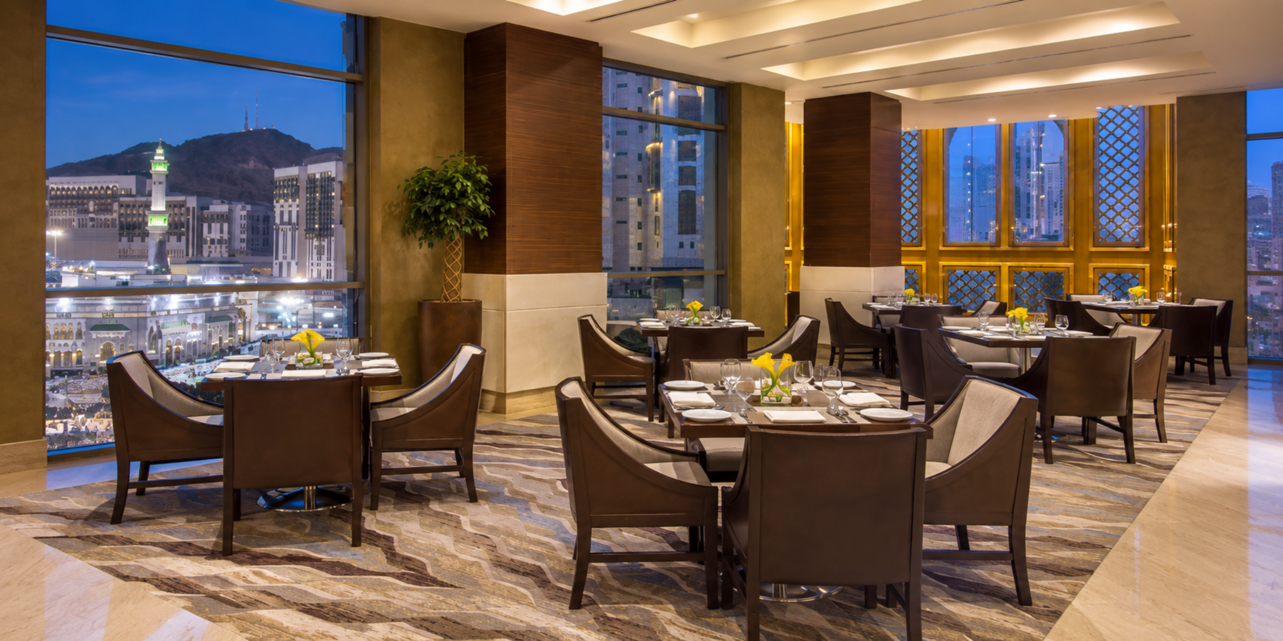 Salle de restaurant élégante du Jabal Omar Hyatt Regency Makkah avec tables dressées et baies vitrées donnant sur le Masjid al-Haram, illustrant les options de restauration adaptées aux pèlerins.