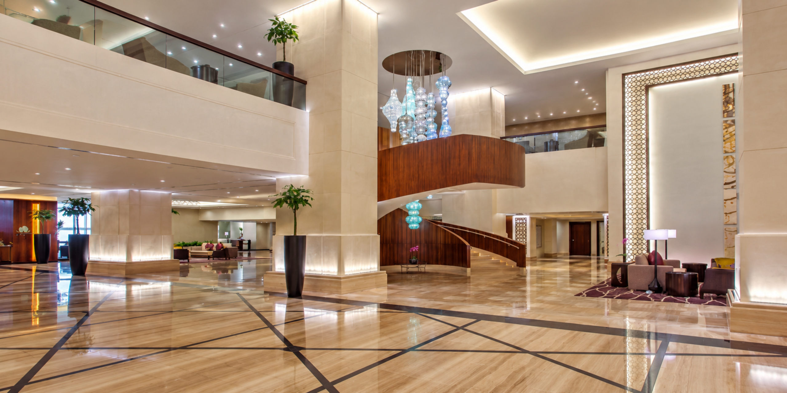 Grand lobby luxueux et spacieux de l'Hôtel Jabal Omar Hyatt Regency Makkah avec escalier en colimaçon, lustres modernes et espaces de réception, illustrant les équipements haut de gamme et l'assistance 24h/24 pour les pèlerins.